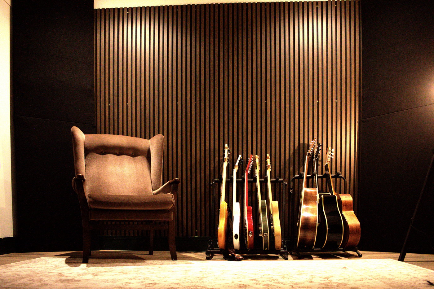 An armchair beside a rack of house guitars against the slatted timber wall at Hot Cat Studios.
